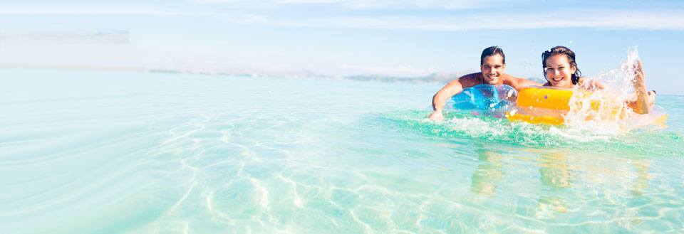 To personer ler og svømmer i krystallklart havvann, holder en fargerik badering.