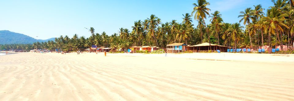 Solfylt strand med palmetrær og fargerike hytter langs strandkanten.