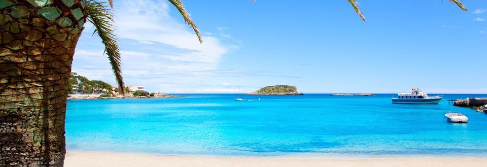 Klar blå himmel over turkis vann ved en tropisk strand med palmetre og båter.