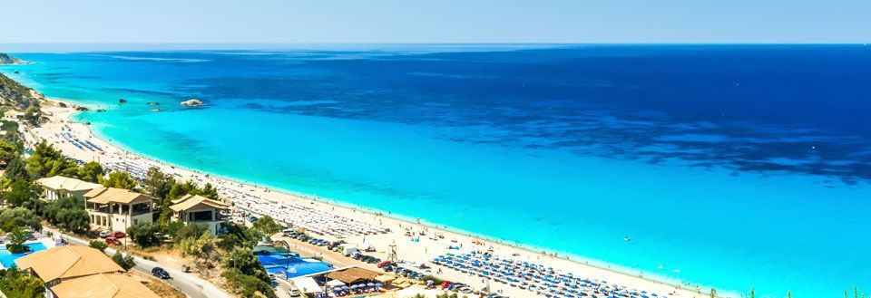 Panorama av en folksom strand med parasoller og krystallklart blått hav.