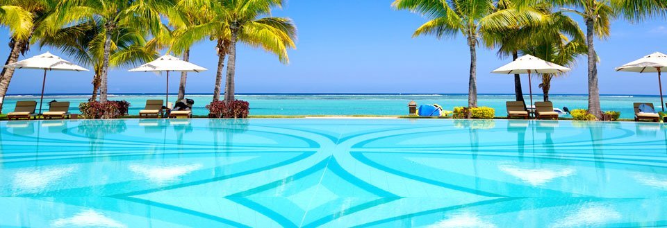 Et tropisk feriested med et svømmebasseng foran havet, omgitt av palmer og parasoller.