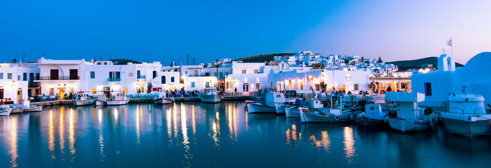 Kveldsbilde av en idyllisk havneby med opplyste bygninger og båter i stille vann.