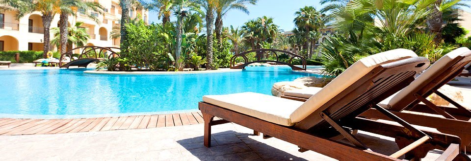 En luksuriøs feriested med svømmebasseng, omkranset av palmetrær og solsenger under en solfylt himmel.