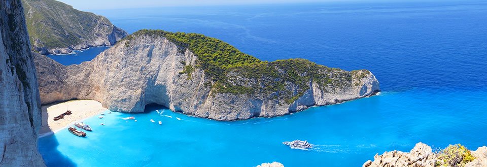 Panoramabilde av en idyllisk bukt med turkisblått vann, omringet av klipper og en strand.