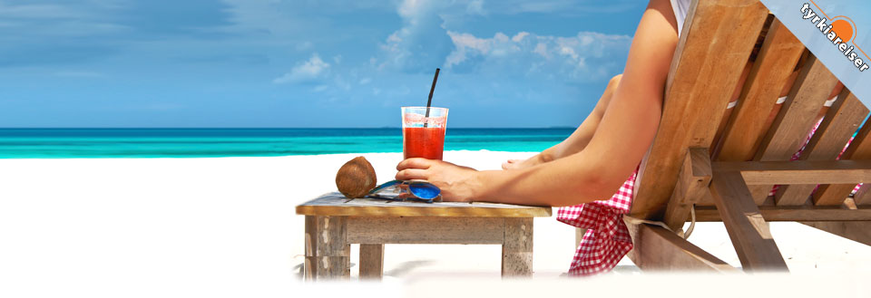 En person hviler i en trebenk på en hvit sandstrand med en drink og en kokosnøtt på et bord.