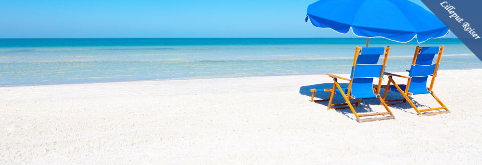 To ledige strandstoler under en blå parasoll på en solrik hvit sandstrand ved et klarblått hav.