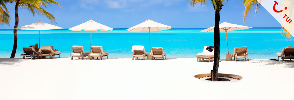 Et tropisk strandlandskap med strålende blå himmel, asurblått hav, hvite sandstrender og solsenger under paraplyer.