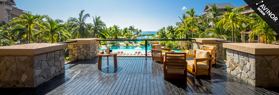 Utsikt fra en luksuriøs balkong med komfortable stoler og utsyn mot et svømmebasseng omkranset av palmer.
