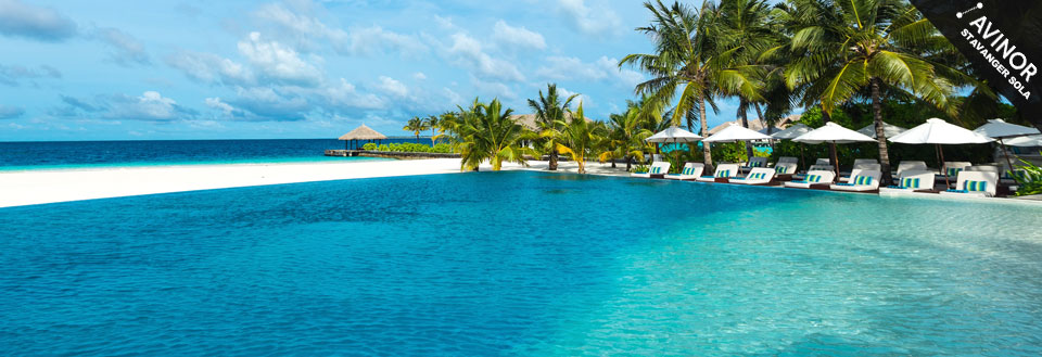 Bildet viser et luksuriøst feriested med en infinity-pool, hvite sandstrender og palmer under en klar blå himmel.