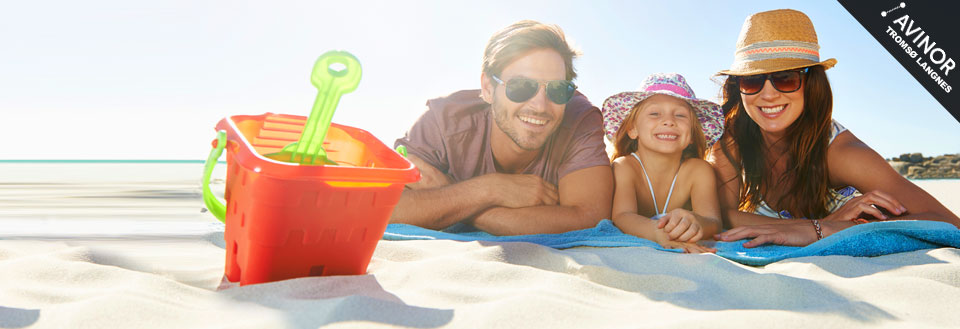 En familie koser seg på en solfylt strand med en lekebøtte i forgrunnen.