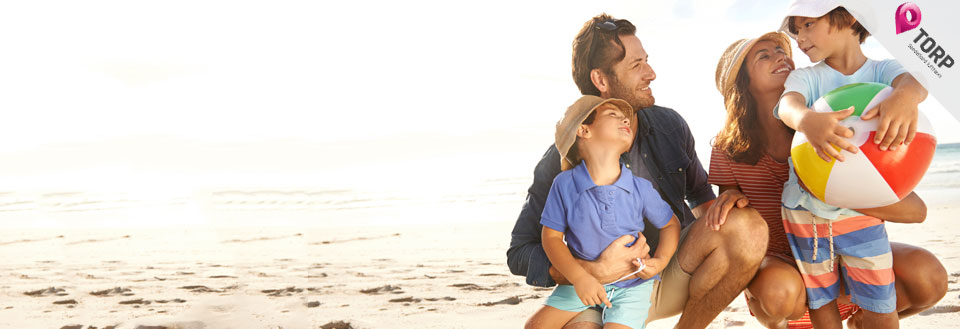 En familie koser seg på stranden i solskinnet med en fargerik strandball.