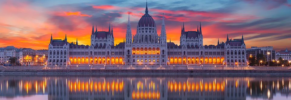 Bildet fremstiller Ungarns parlamentsbygning i Budapest ved solnedgang, reflektert på vannoverflaten.