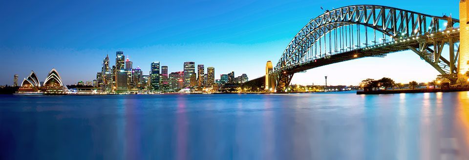 Panoramabildeover Sydney med Sydney Bridge og Utzons operahus i tusmørke.