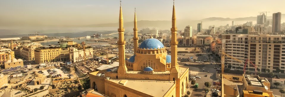 Bilde av en bysilhuett med en dominerende moské og to gylne minareter under en klar himmel.