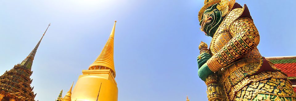 Grand Palace i Bangkok med gylne spir og en stor dekorert statue.