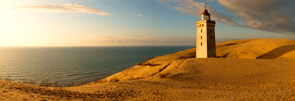 Rubjerg Knude fyrtårn ved kysten, omringet av sanddyner i den gyldne solnedgangen.