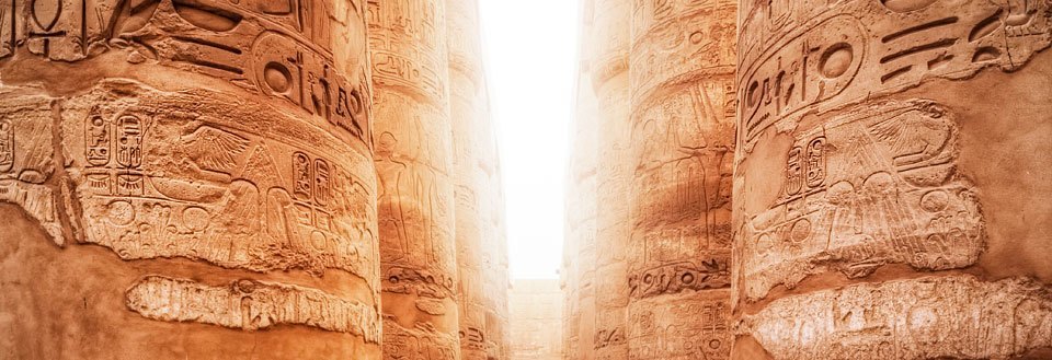 Bildet fremviser gamle hieroglyfer på søylene inne i et egyptisk tempel i gyllent lys.
