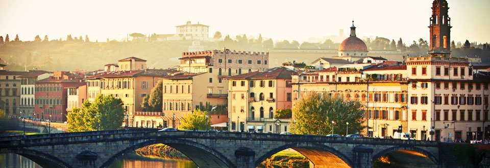 Solnedgång över Arnofloden i Florens med en stenbro i förgrunden och historiska byggnader i bakgrunden.