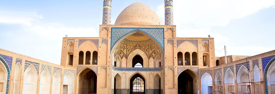 Eldgammel moské med imponerende buer og detaljert flisearbeid under en klar blå himmel.