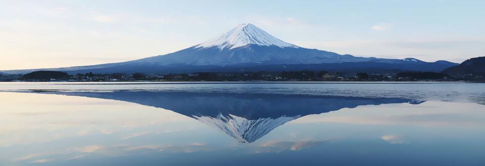 Det ikoniske Fuji-fjellet i Japan og dets perfekte speilbildet i vann under solnedgang.