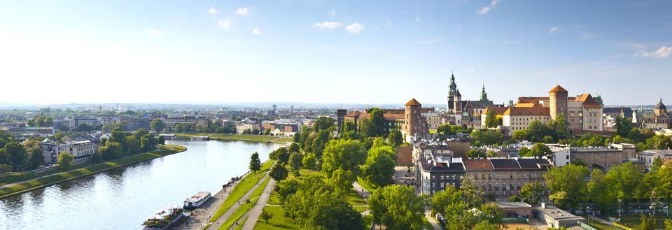 Panoramautsikt over en europeisk by med historiske bygninger og et slott ved en elv, omkranset av grøntarealer.