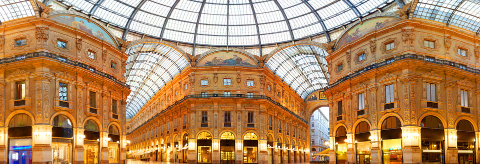 Innvendig panorama av prangende glasskuplet konstruksjon med elegante buer og butikker.