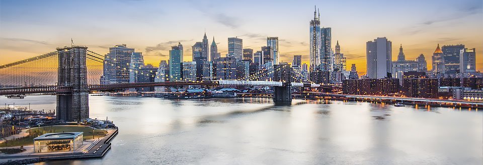 Brooklyn Bridge og Manhattans silhuett i skumringen, med belyste bygninger.