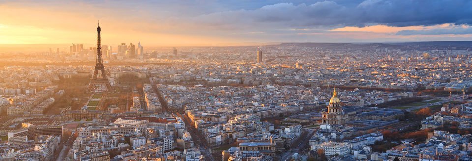 Panorama av Paris i solnedgang, med Eiffeltårnet og tett bybebyggelse.