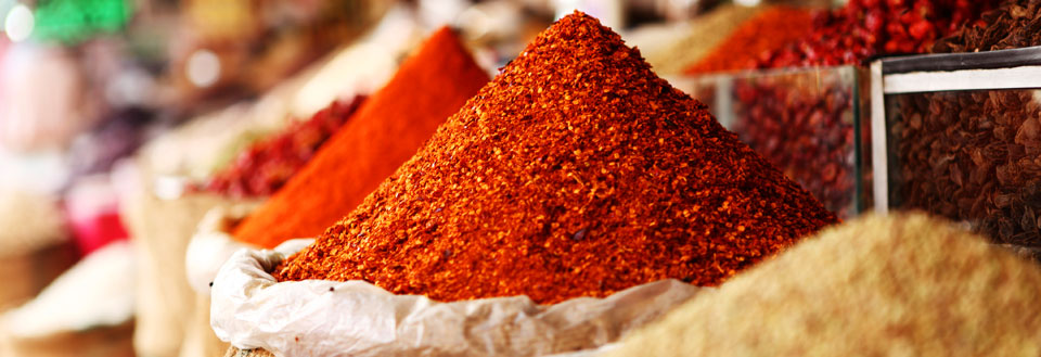 Fargerike hauger av krydder på et marked, praktfull rød og brun fargetoner.