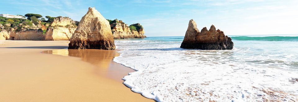 En solfylt strand med gyllen sand og klippeformasjoner som stiger opp fra vannet.