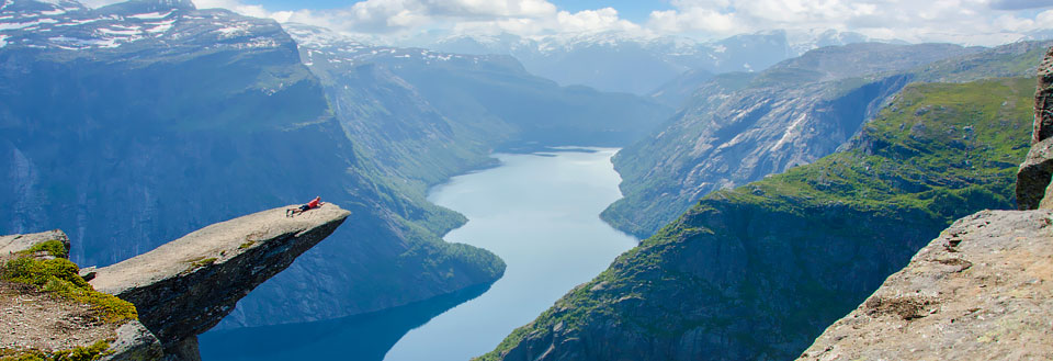 En person ligger på kanten av Trolltunga med beina strukket ut over en storslagen fjord.