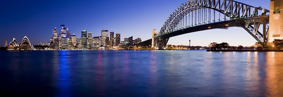 Sydneys skyline med en kjent buebro og refleksjoner i vannet.