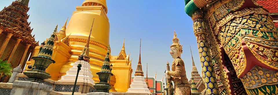 Grand Palace i Bangkok med gyldne stupaer, fargerike mosaikker og tradisjonelle statuer under en klar blå himmel.
