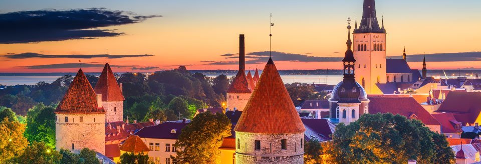 Tallinn ved solnedgang med tårn og kirketårn, under en himmel med fargerike nyanser.