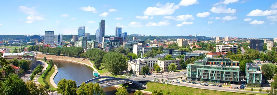 Panoramautsikt over Vilnius med moderne byggverk, en elv og en bro under en klar blå himmel.