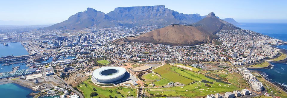 Panoramautsikt over Cape Town med stadion, havneanlegg og et fjell i bakgrunnen.