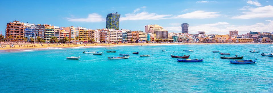 Solskinnsdag ved Gran Canarias kyst med fargerike leilighetskomplekser og småbåter på det klare havet.