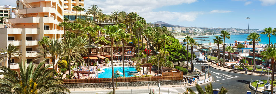 Livlig ferieanlegg med svømmebasseng, omringet av palmetrær, og en klar blå himmel.