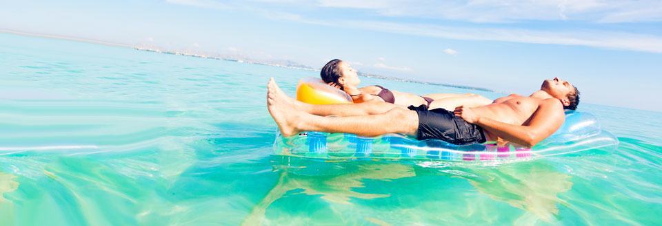 To personer hviler seg på en flytende luftmadrass i et stille hav under en klar himmel.