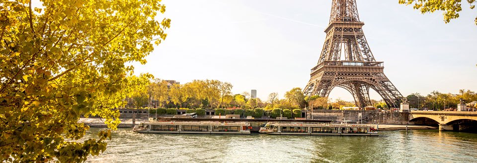 Eiffeltårnet troner i Paris' silhuett langs Seinen med en elvebåt, som seiler forbi under klar himmel.