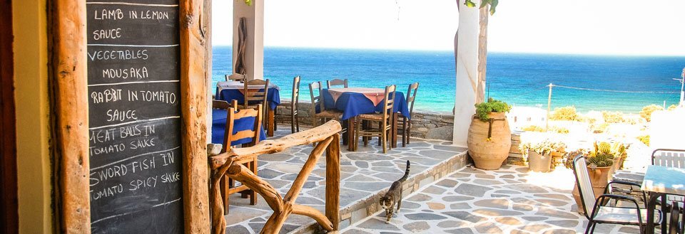 Koselig terrasse ved sjøen med en meny på en tavle og bord og stoler.