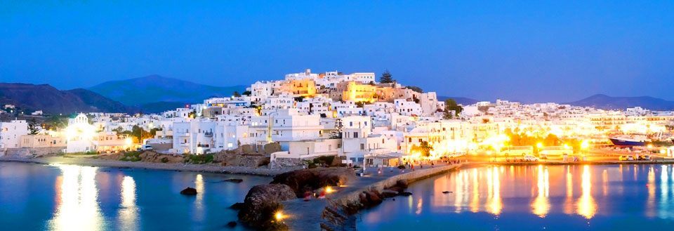 En pittoresk kystby på Naxos i skumringen med opplyste hvite bygninger og reflekterende vann.