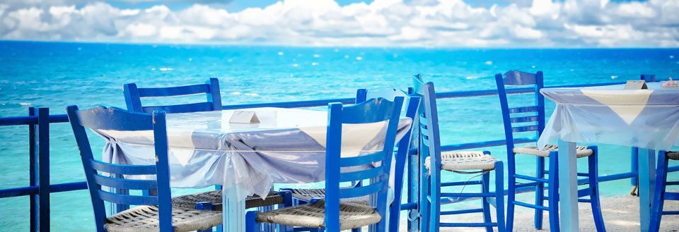 Et koselig uteserveringsområde med blå stoler foran en vakker sjøutsikt.