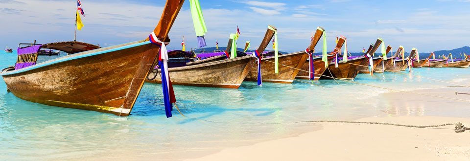 Tradisjonelle Phuket trebåter med fargerike bånd fortøyd på en tropisk strand med krystallklart vann.