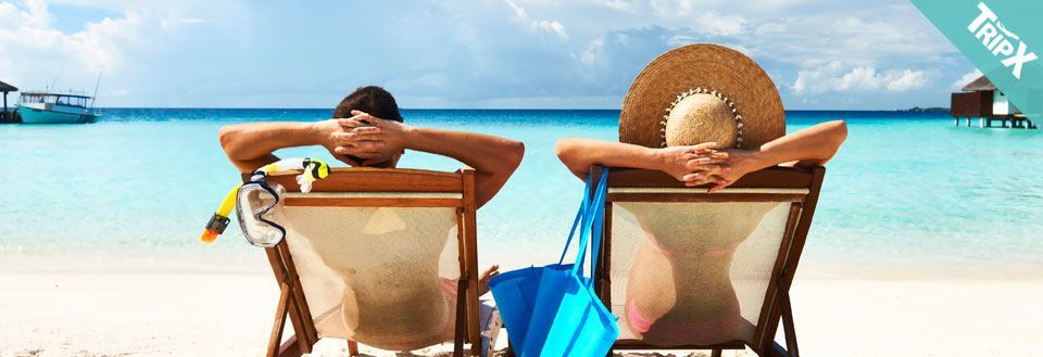 To personer avslapper på solstoler ved en krystallklar strand, med dykkeutstyr ved siden av.