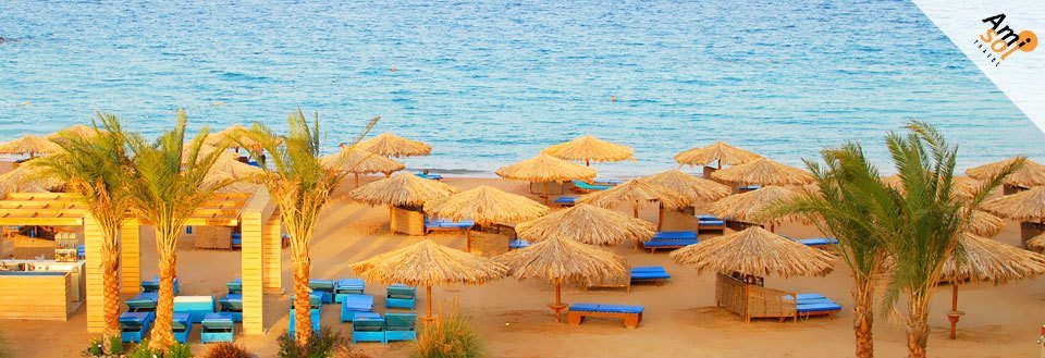 En solfylt strandlinje med stråparasoller og blå solsenger mot en bakgrunn av klart blått hav.