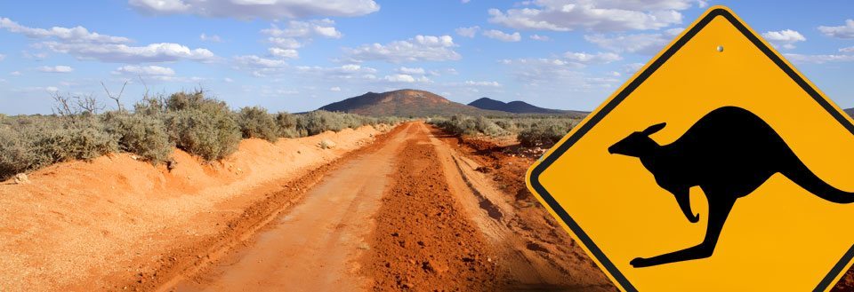 Rød jordvei som strekker seg mot et fjell under en blå himmel, med kanguruskilt.