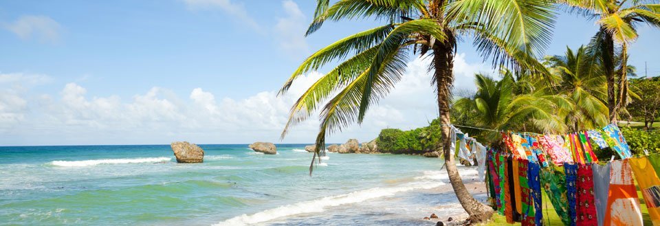 Tropisk strand med klar blå sjø, palmer og fargerikt tøy hengt opp til tørk.