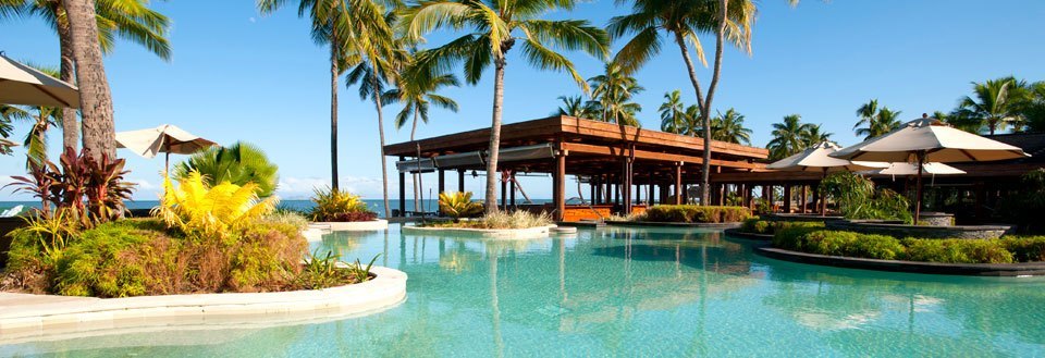 Luksuriøst feriested med svømmebasseng omkranset av palmetrær og solsenger under parasoller.