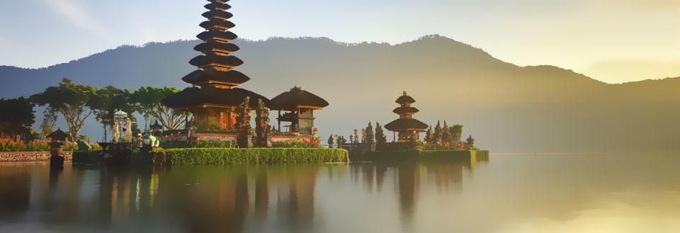 Et fredfullt tempel ved en innsjø med fjell i bakgrunnen ved soloppgang.